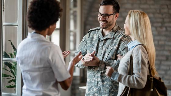 Happy army soldier and his wife communicating with African American healthcare worker while having consultations at the clinic.